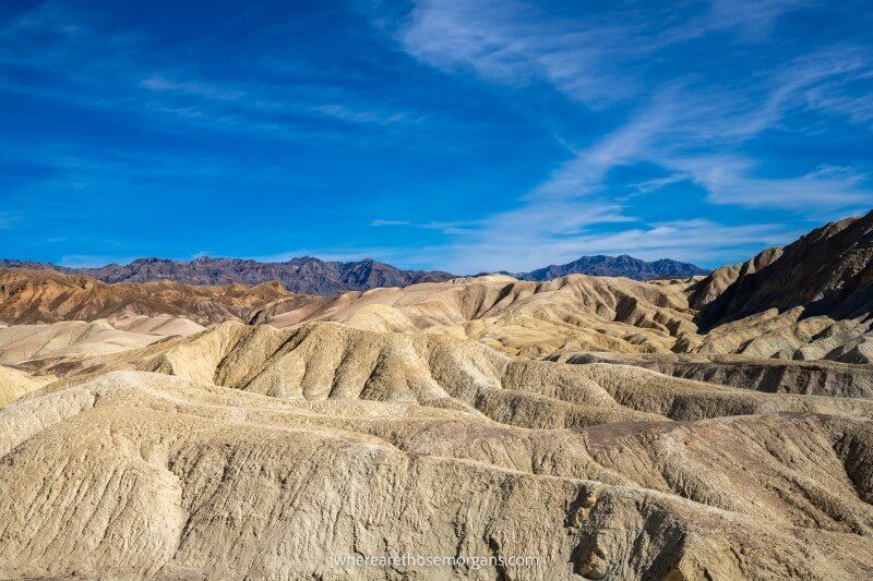 Rolling mounds leading to tall mountains and a blue sky at Golden Canyon in Death Valley