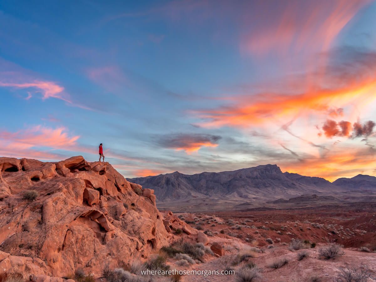 Stunning sunset with hiker stood on rock formation in Valley of Fire State Park near Las Vegas Nevada photographing swirling colors in the clouds at dusk one of the best things to do in the park