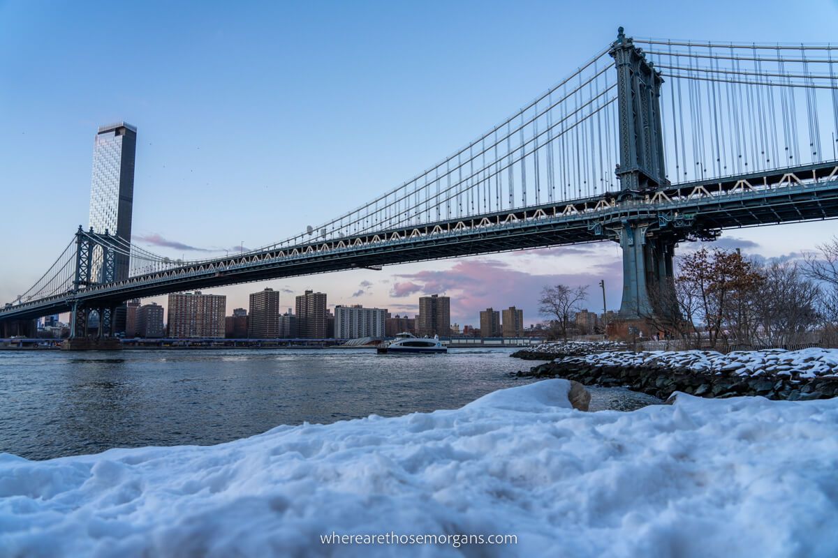 Manhattan Bridge green blue color with snow on the ground in Brooklyn at dusk