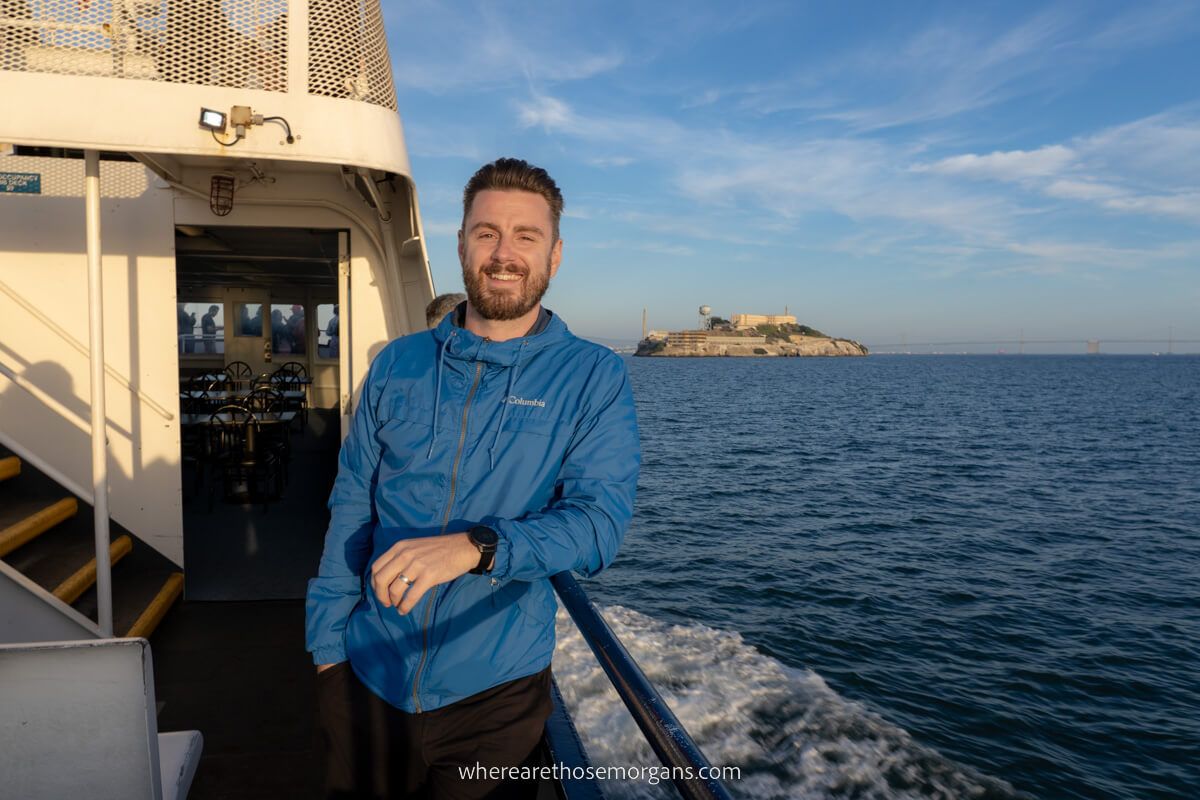 Man standing on the side of a boat with Alcatraz Island in the background