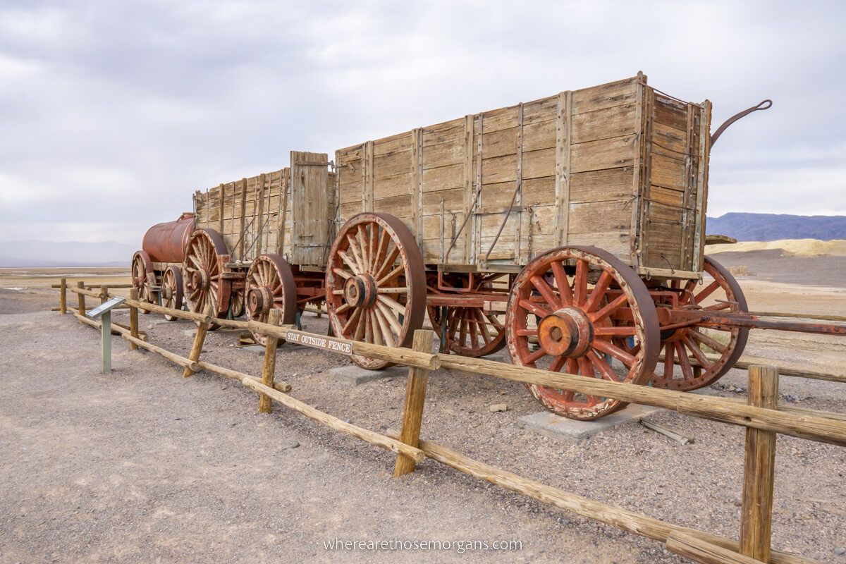 Old historic train engine with two large wooden wagons behind on display in the middle of a huge desert