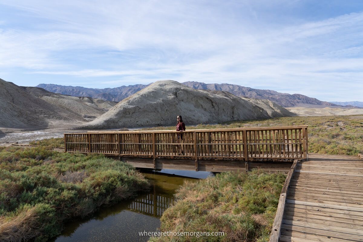 Tourist walking across wooden bridge over a shallow creek in the middle of a desert in California