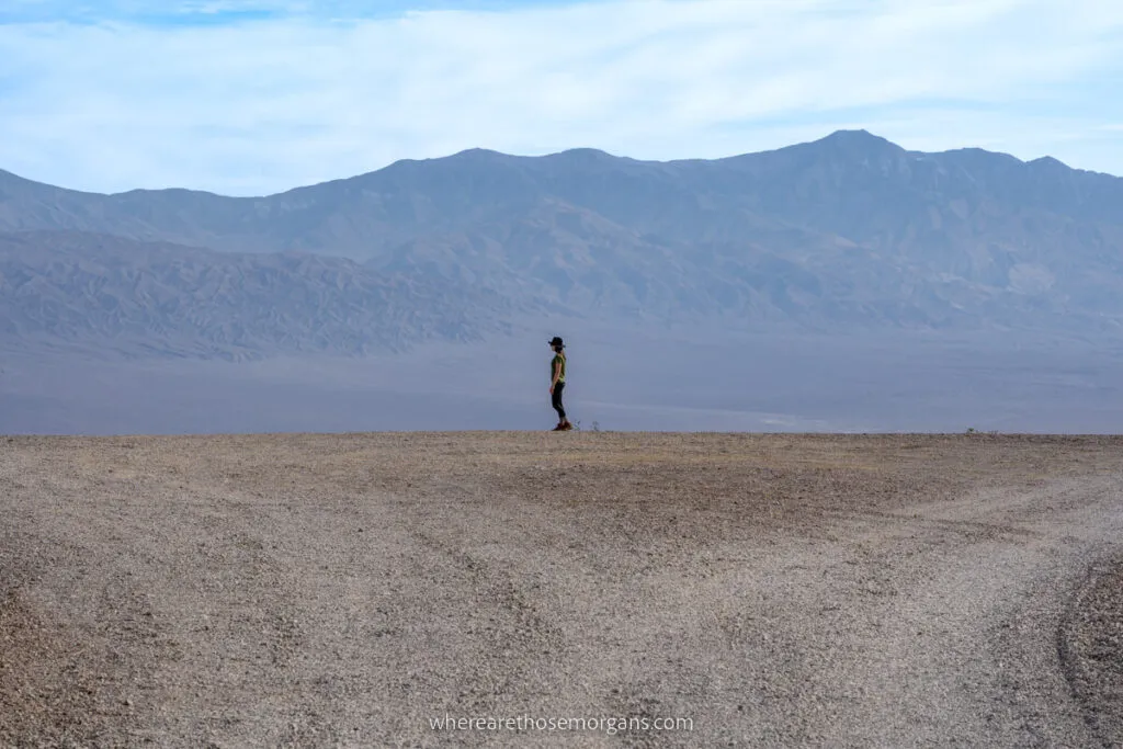 Woman stood small in the distance against mountains in the desert