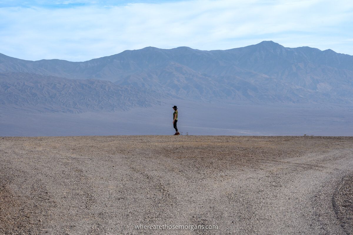 Telephoto picture of a tourist stood on the edge of a road with a gigantic desert and mountains behind