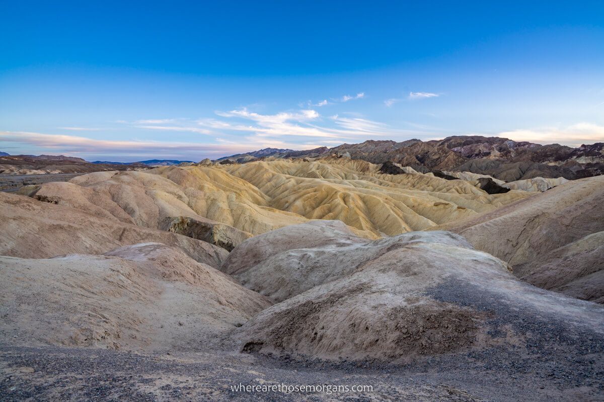 Colorful mounds undulating through a wide open landscape leading to mountains and light clouds in the sky