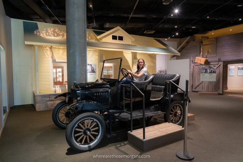 Woman sitting in a car in an exhibit in the History Colorado Center