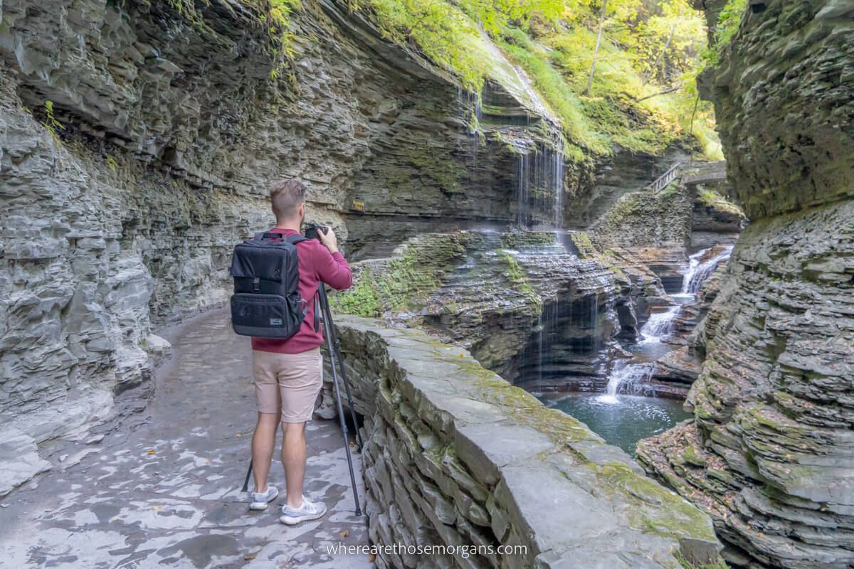Man taking a photo of a waterfall with a tripod and a backpack