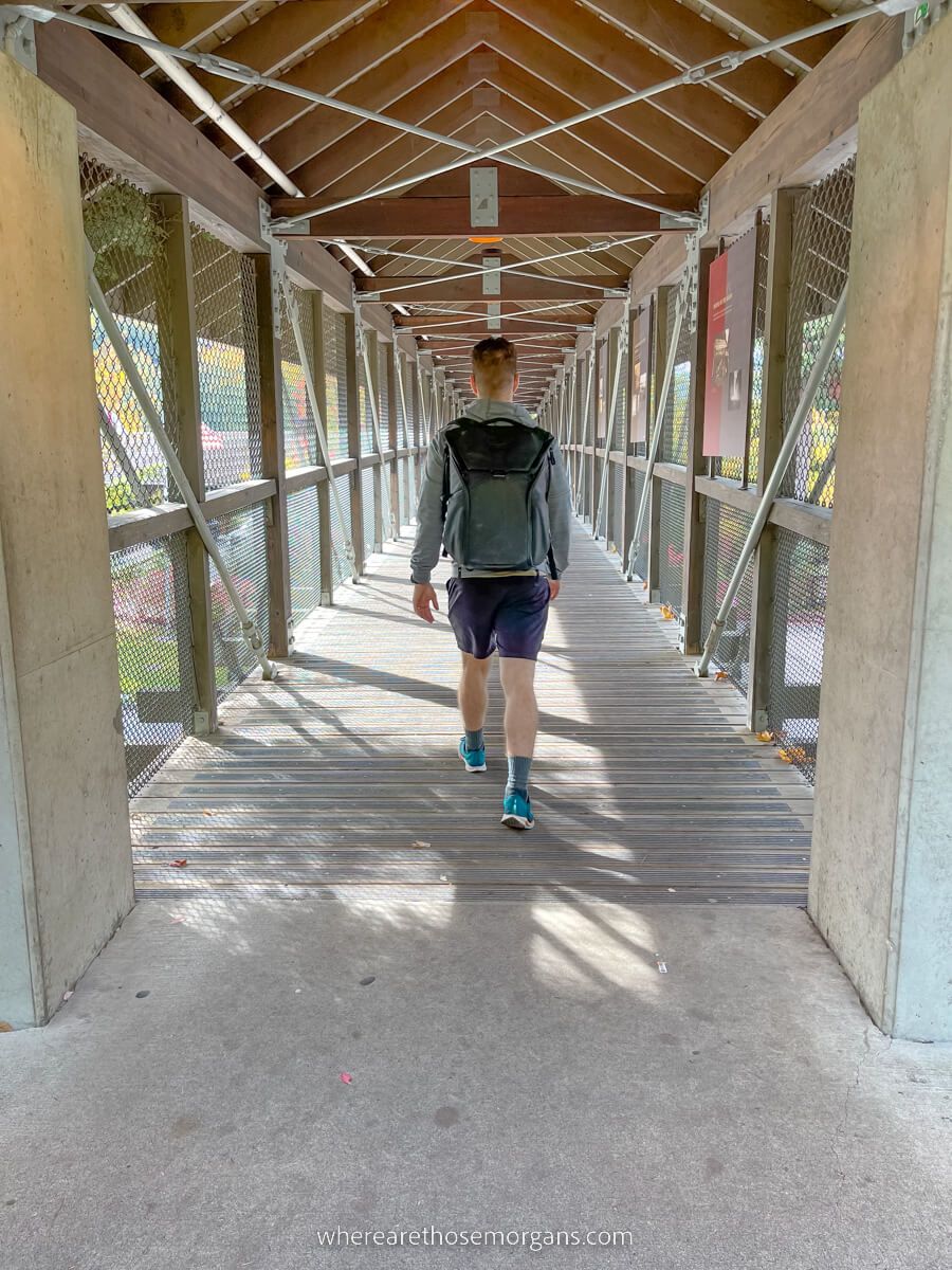 Person walking through a wooden footbridge tunnel with backpack