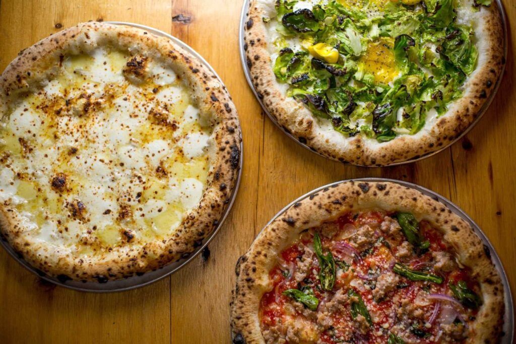 Three Neapolitan pizzas sitting on a wooden table