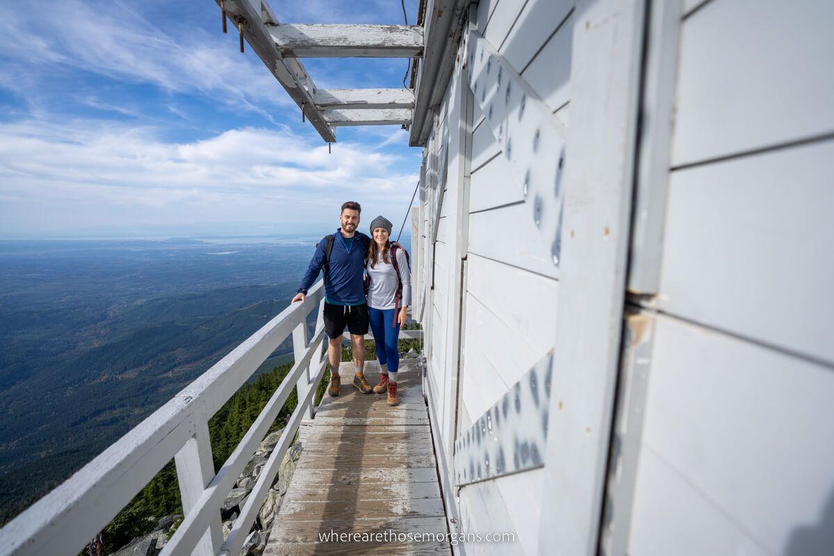 Mark and Kristen Morgan from Where Are Those Morgans together on the outside of Mt Pilchuck Lookout with far reaching views to one side over Washington State