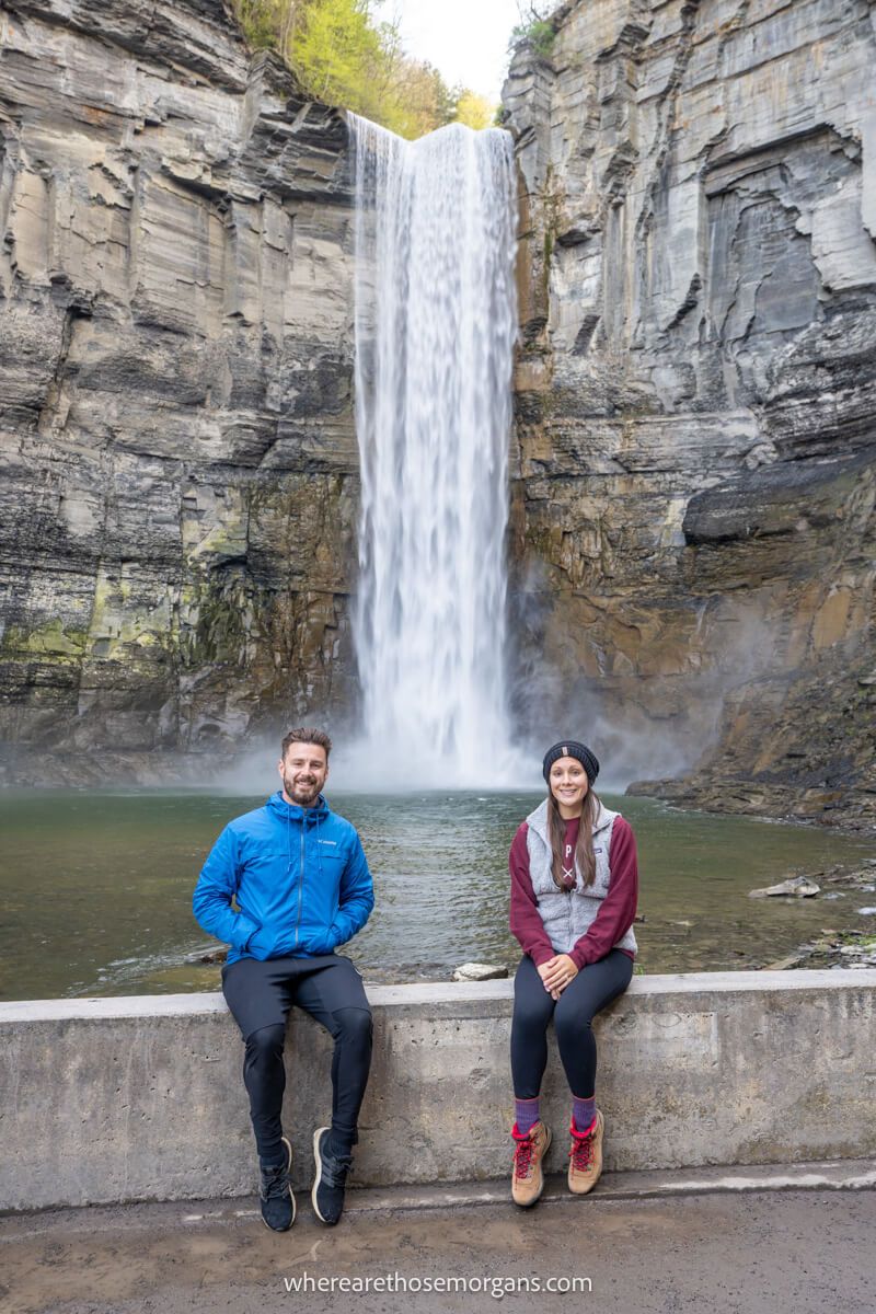 Two people sitting on a stone wall in front of a waterfall