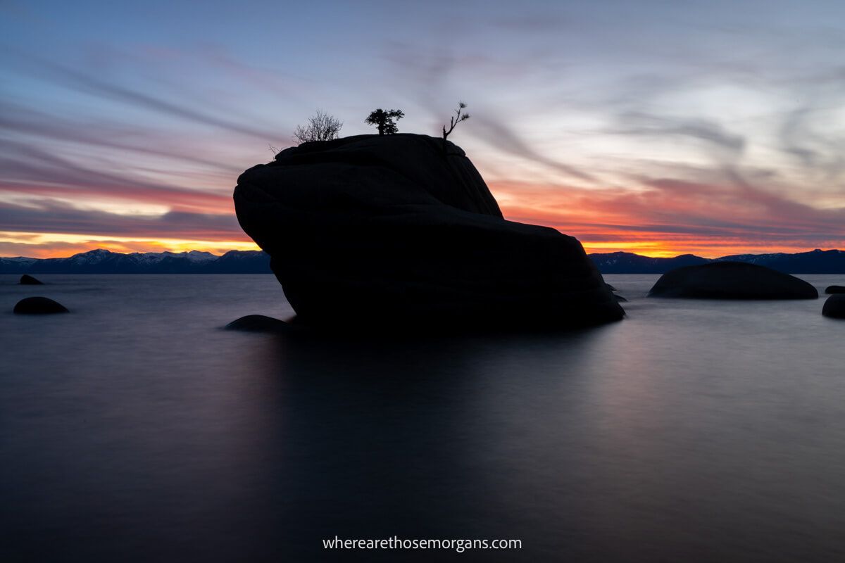 Huge rock out in the water silhouetted against a colorful sunset