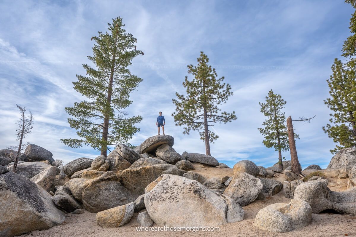Hiker standing on top of large boulders on a beach with some trees to either side