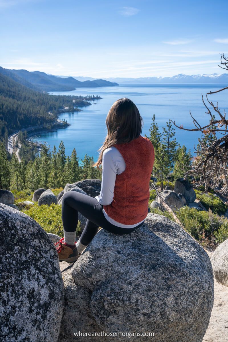 Hiker sat on a boulder looking out at a far reaching view over a lake and mountains from an elevated vantage point