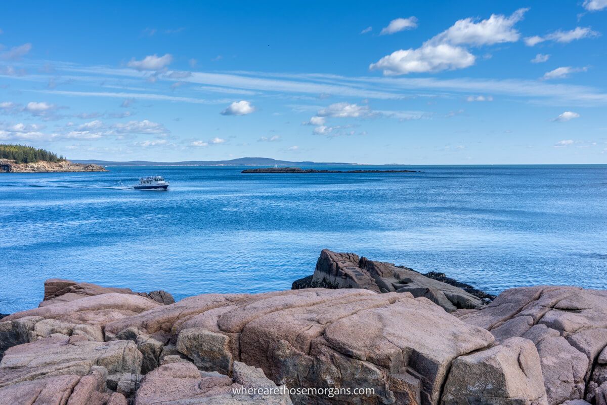 View from large boulders overlooking a white boat slowly cruising on an inlet in the ocean near the Maine coastline