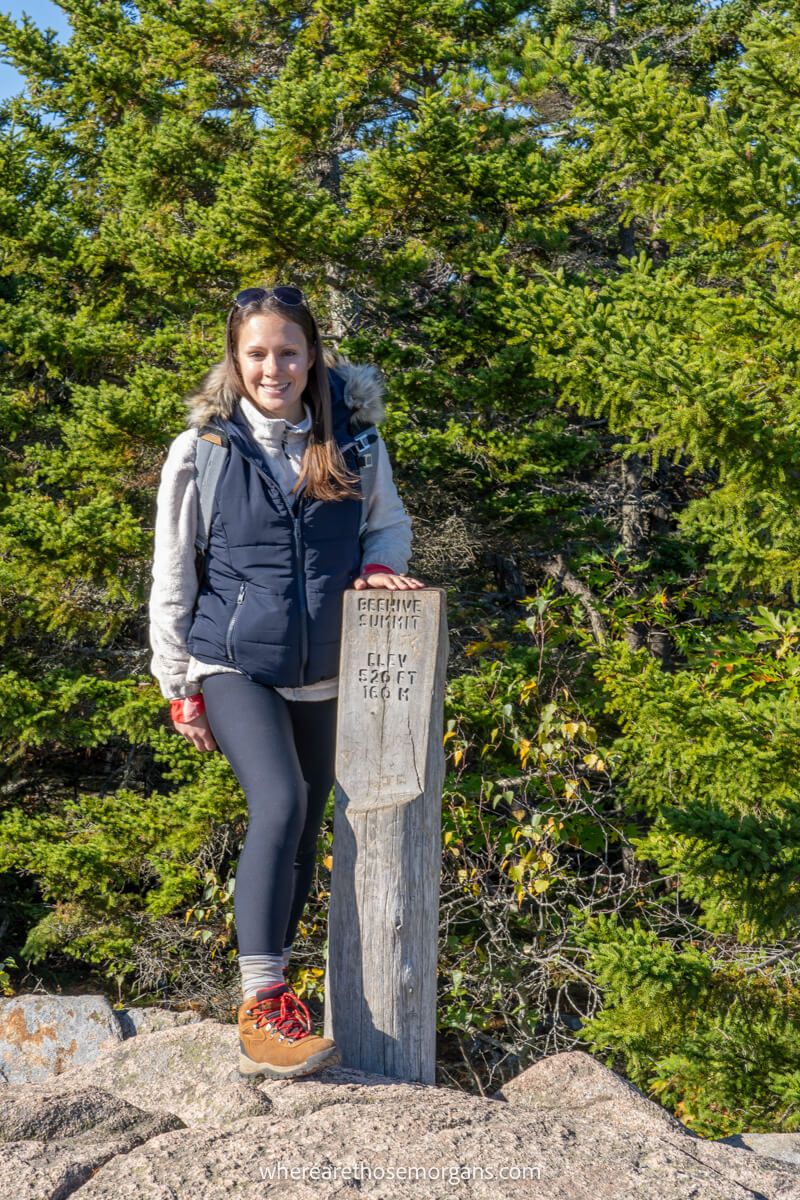 Hiker smiling for a photo next to the Beehive Trail summit marker in Acadia