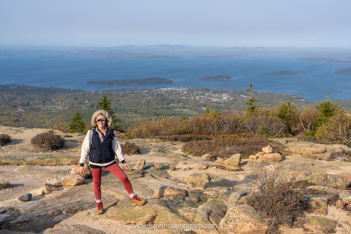 Hiker stood on a rocky plateau at the summit of Cadillac Mountain in Acadia with wide open and far reaching views over the ocean behind