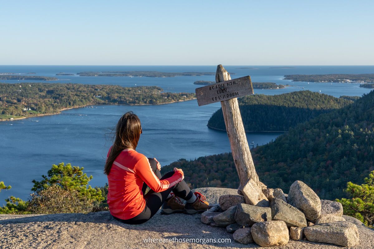 Hiker sat enjoying the views over lakes from a mountain summit marker
