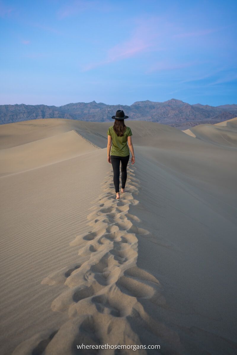 Tourist in a hat walking on the crest of a sand dune and leaving footsteps at dusk