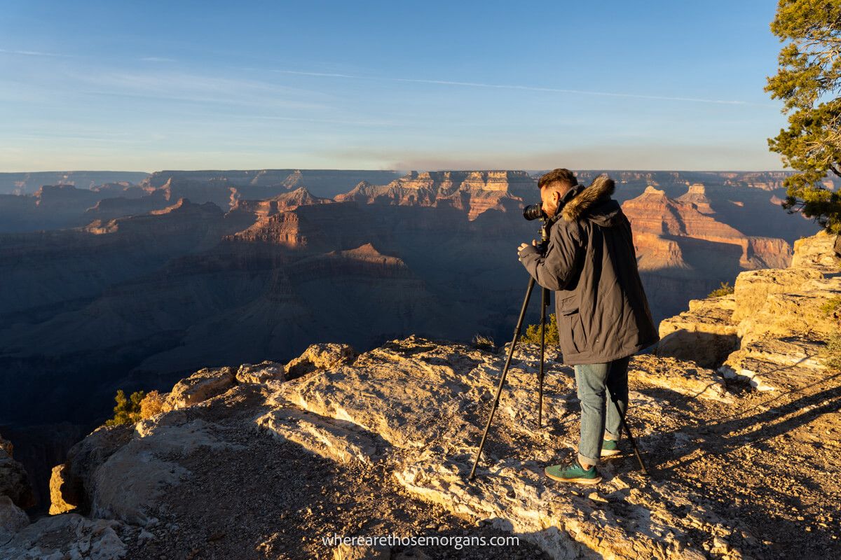 Tourist in winter coat standing with a tripod and camera at sunset in the Grand Canyon