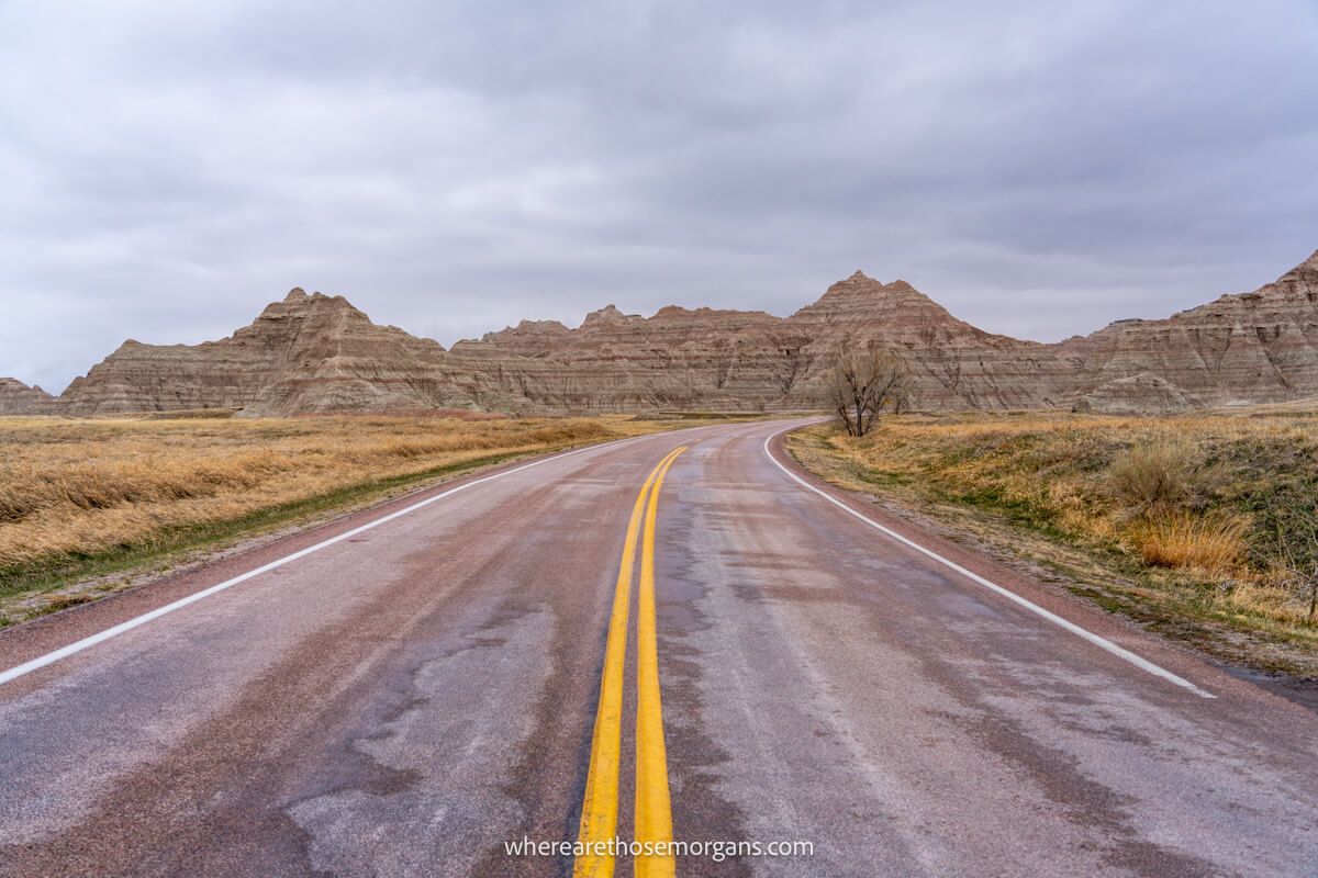 Photo of an empty road slightly curving and disappearing into rock formations with thick clouds in the sky