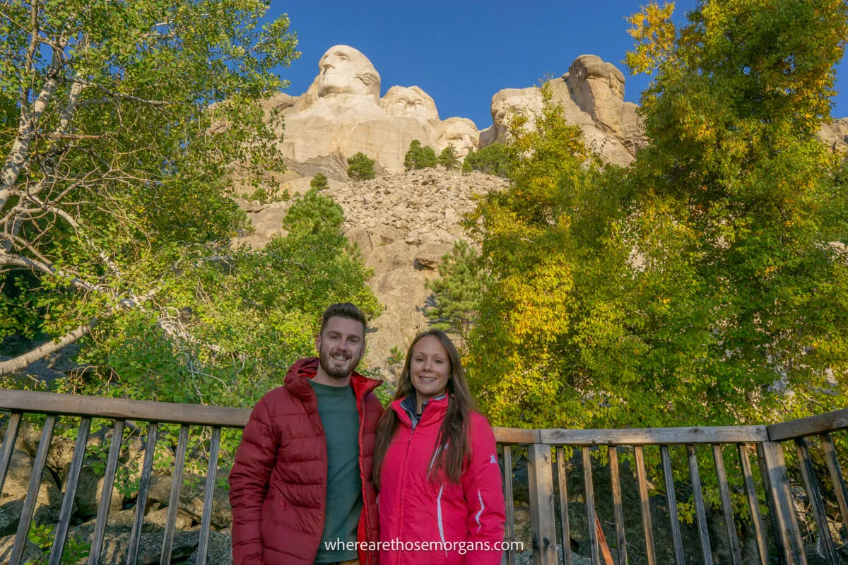 Photo of a couple with trees and a gap to a granite carving on a mountain behind