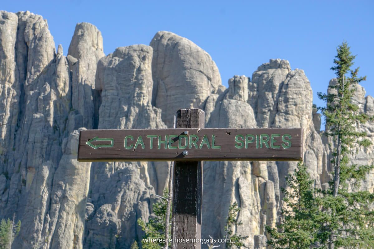 Wooden sign showing left turn to Cathedral Spires hike with towering granite rocks behind