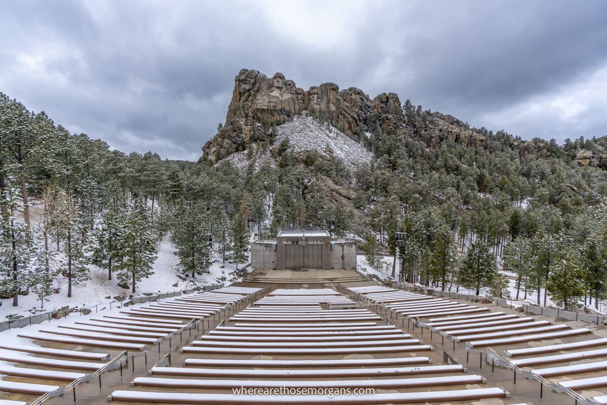 Wide angle photo showing an empty Lincoln Borglum amphitheater overlooking Mount Rushmore with snow on the ground and clouds in the sky