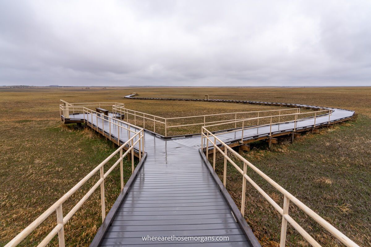 Wooden boardwalk jutting out into a wide open prairie with heavy clouds above