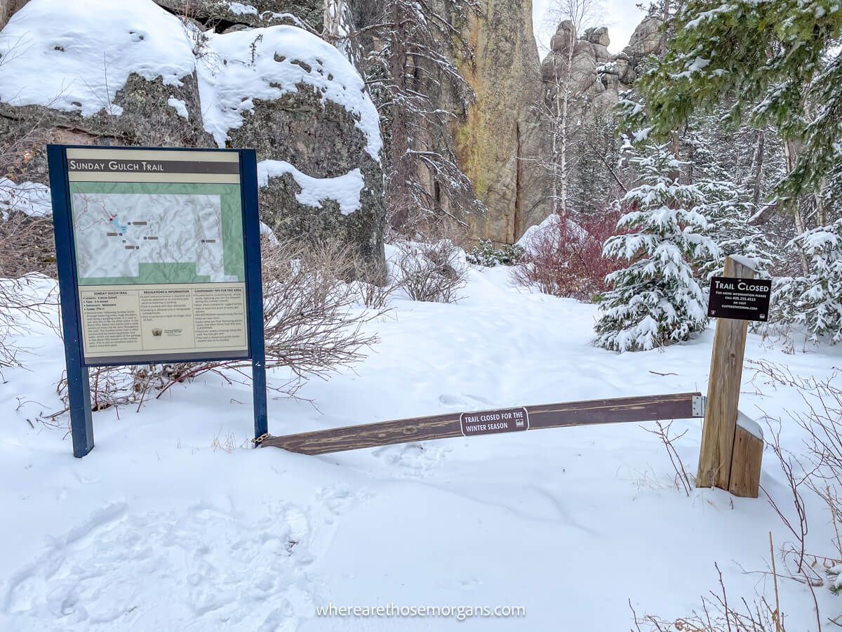 Hiking trailhead covered in snow with a trail closed sign