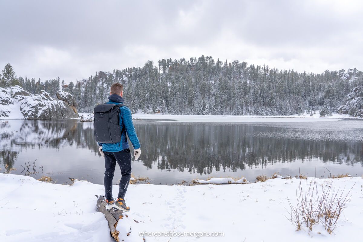 Hiker standing on a rock overlooking a lake with lots of snow on the ground and snow clouds in the sky