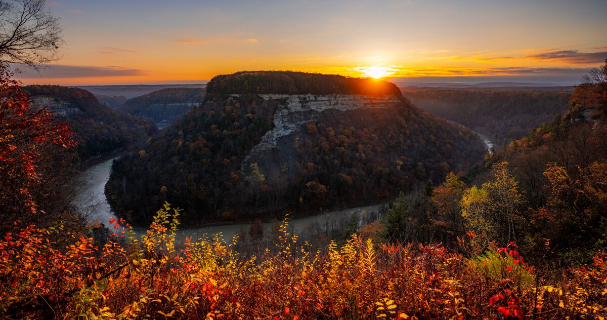 Sunrise over a horseshoe shaped river and cliffs with fall foliage colors lighting up