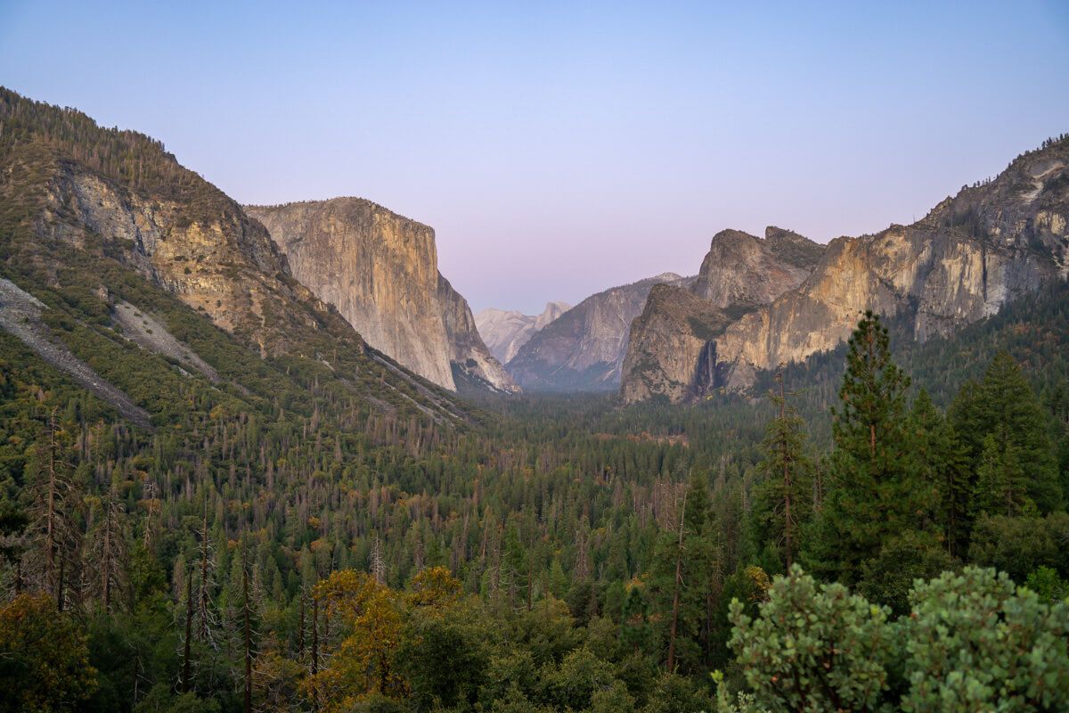 Famous view of Yosemite National Park at dusk with purple and blue sky over trees and granite rocks