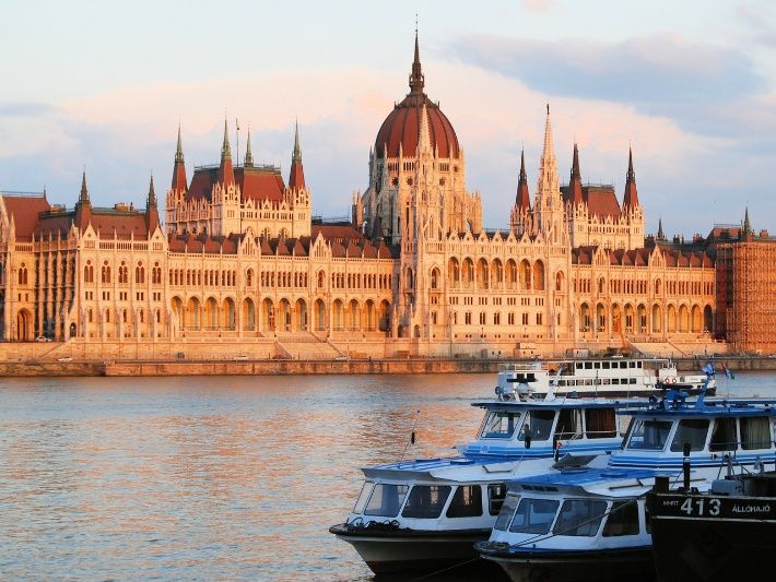 Boats moored on the River Danube with Budapest Parliament building on the far side of the river at dawn