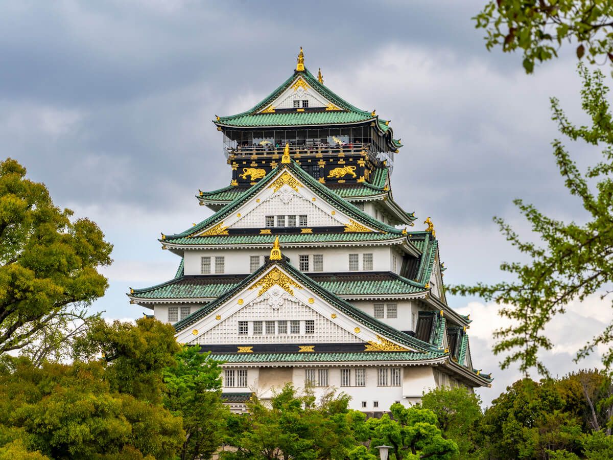 Osaka Castle in Japan with clouds behind and green leaves in front