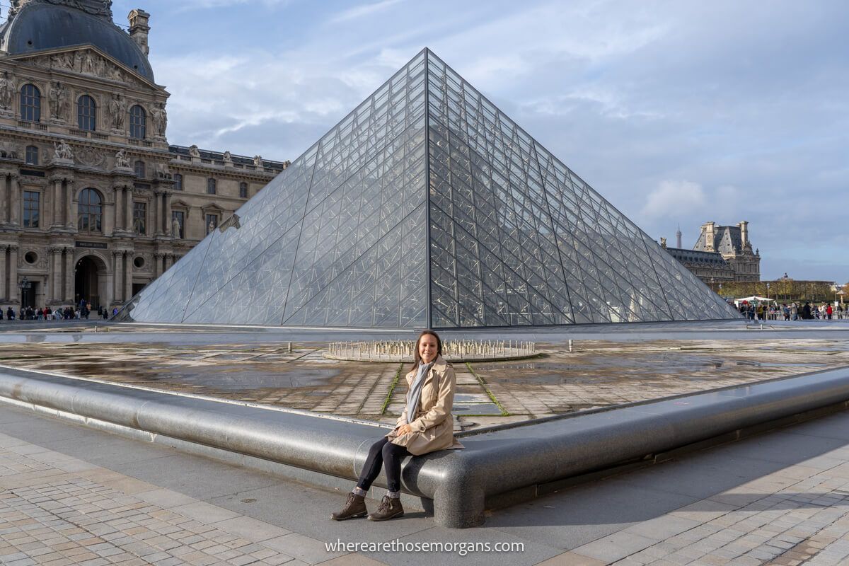 Tourist sat in front of a glass pyramid within a courtyard in Paris
