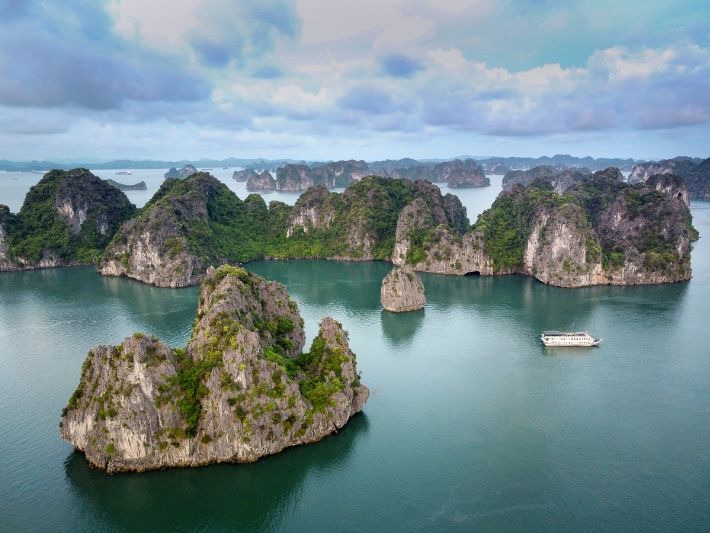 Elevated photo overlooking Ha Long Bay in Vietnam with limestone karsts bursting out of the water and a single cruise boat floating
