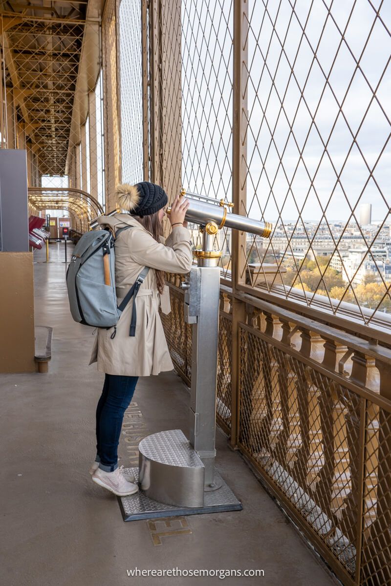 Woman looking out through a silver telescope on the first floor of the Eiffel Tower in Paris, France