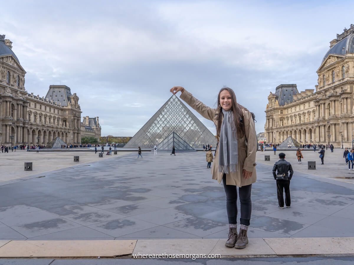 Woman pinching the top of the glass pyramid to the Louvre