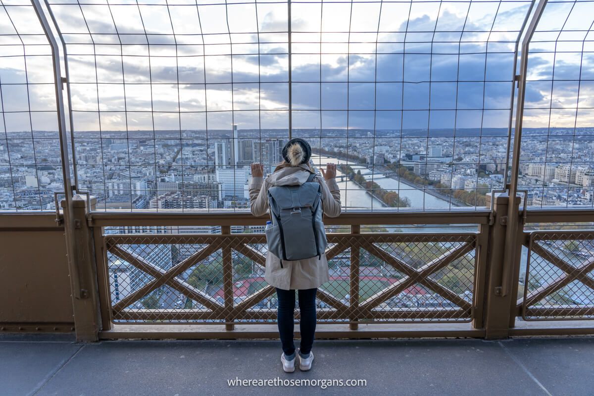 Woman looking out through metal fencing at the third floor of the Eiffel Tower
