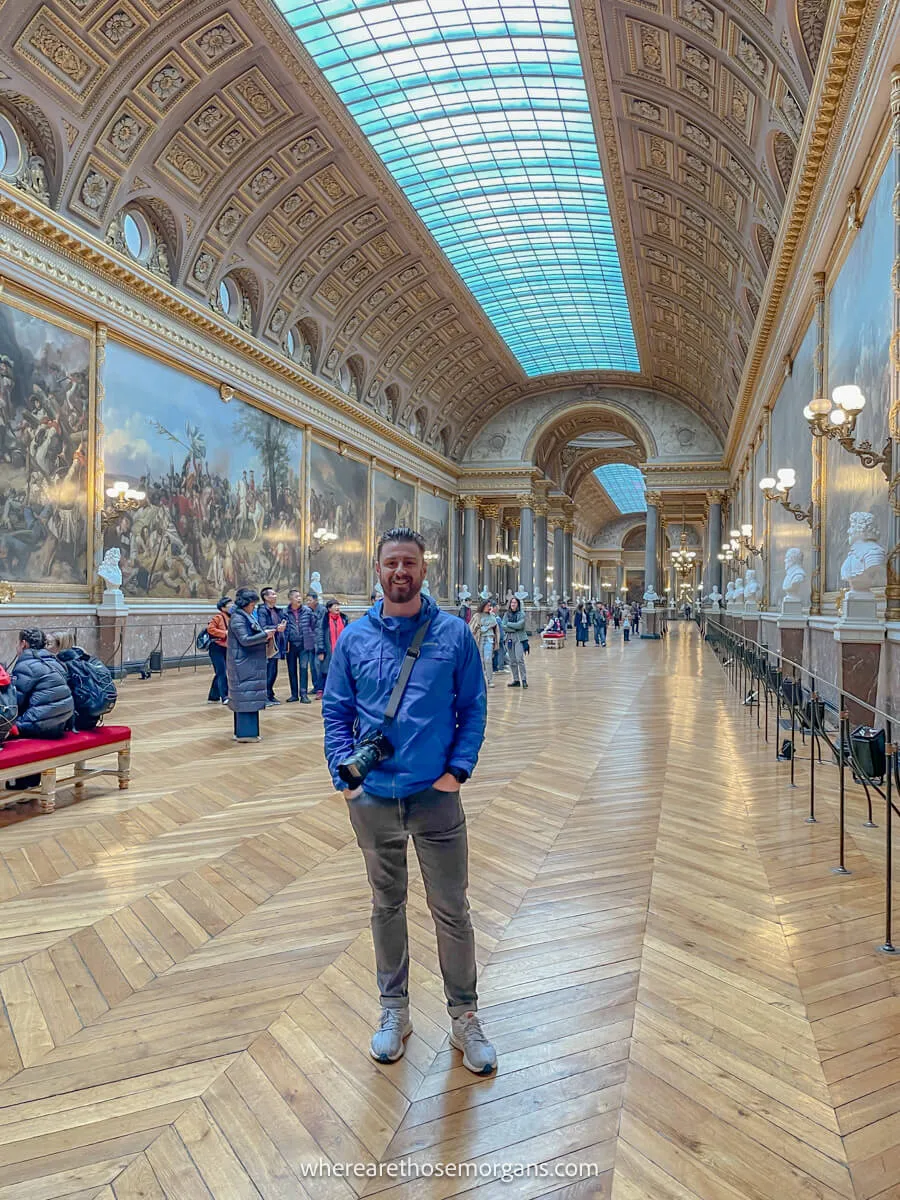 Man posing for a photo inside a large hall at the palace of versailles