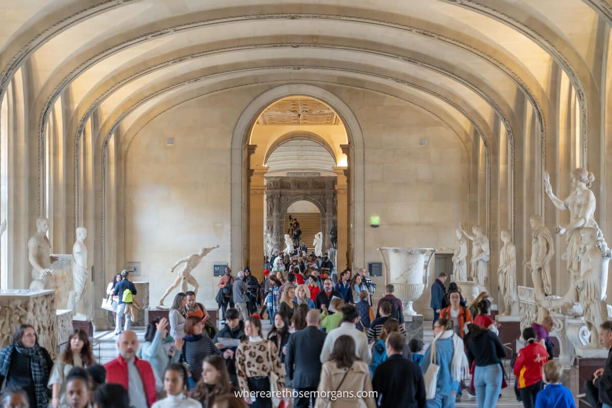 Numerous visitors walking through one of the large halls inside the Louvre