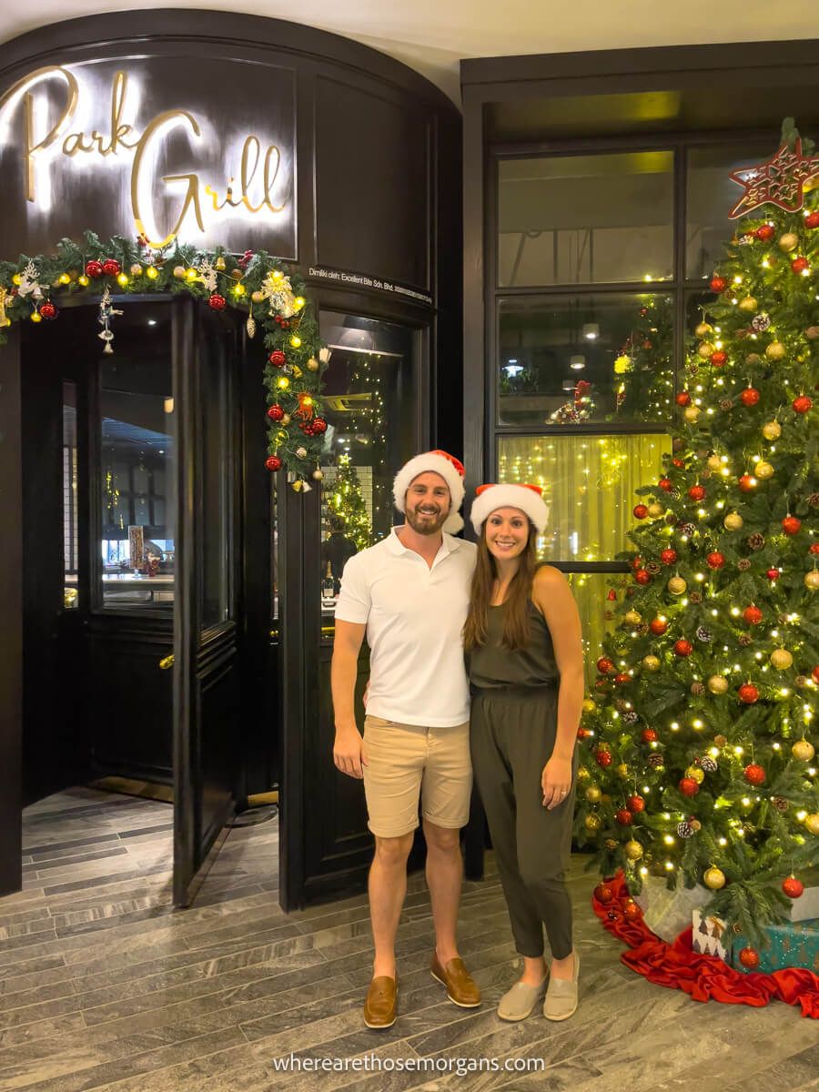 Photo of a couple standing together with santa hats next to a christmas tree outside a high end restaurant in Kuala Lumpur