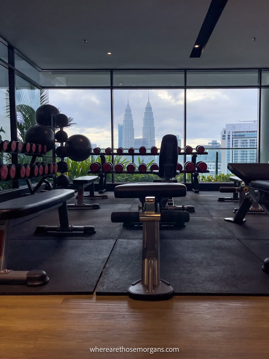 Photo of a gym with benches and free weights leading to city views through large glass windows