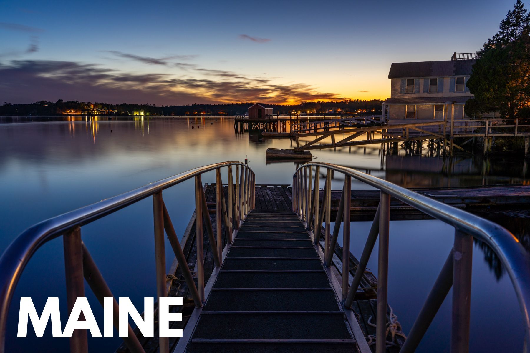 Pier leading out into a still bay at sunset with a colorful sky above and the word Maine overlaid