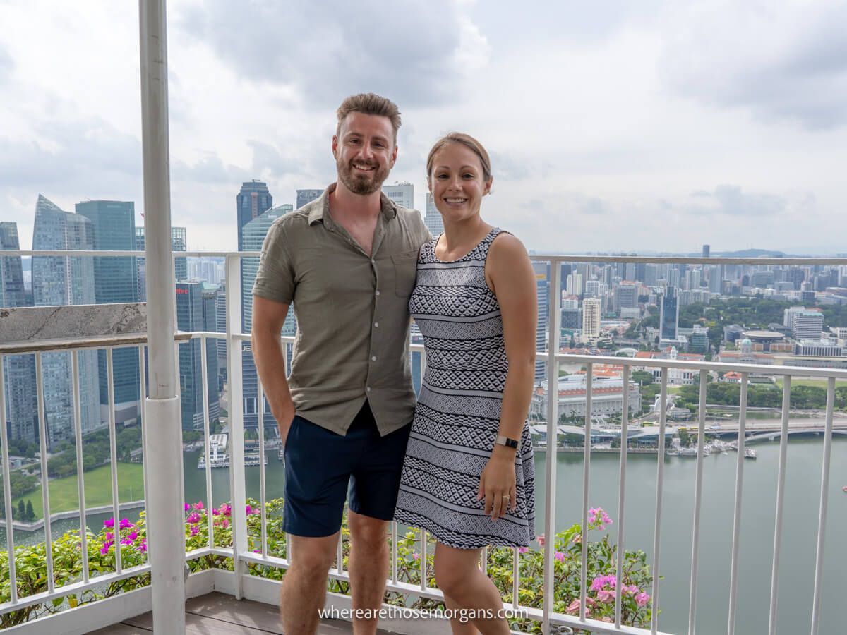 Photo of a couple standing together on a rooftop with views of a city in the background on a cloudy day