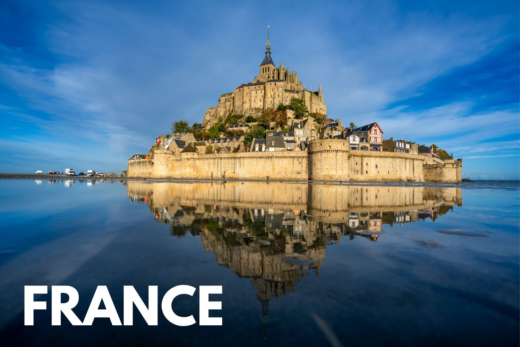 Photo of Mont St Michel walled city reflecting in shallow water on a beach in France