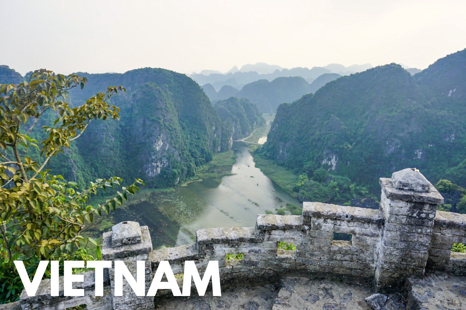 Photo of a stone staircase with a wall leading to views over a river leading between limestone karsts on a cloudy day with the word Vietnam overlaid