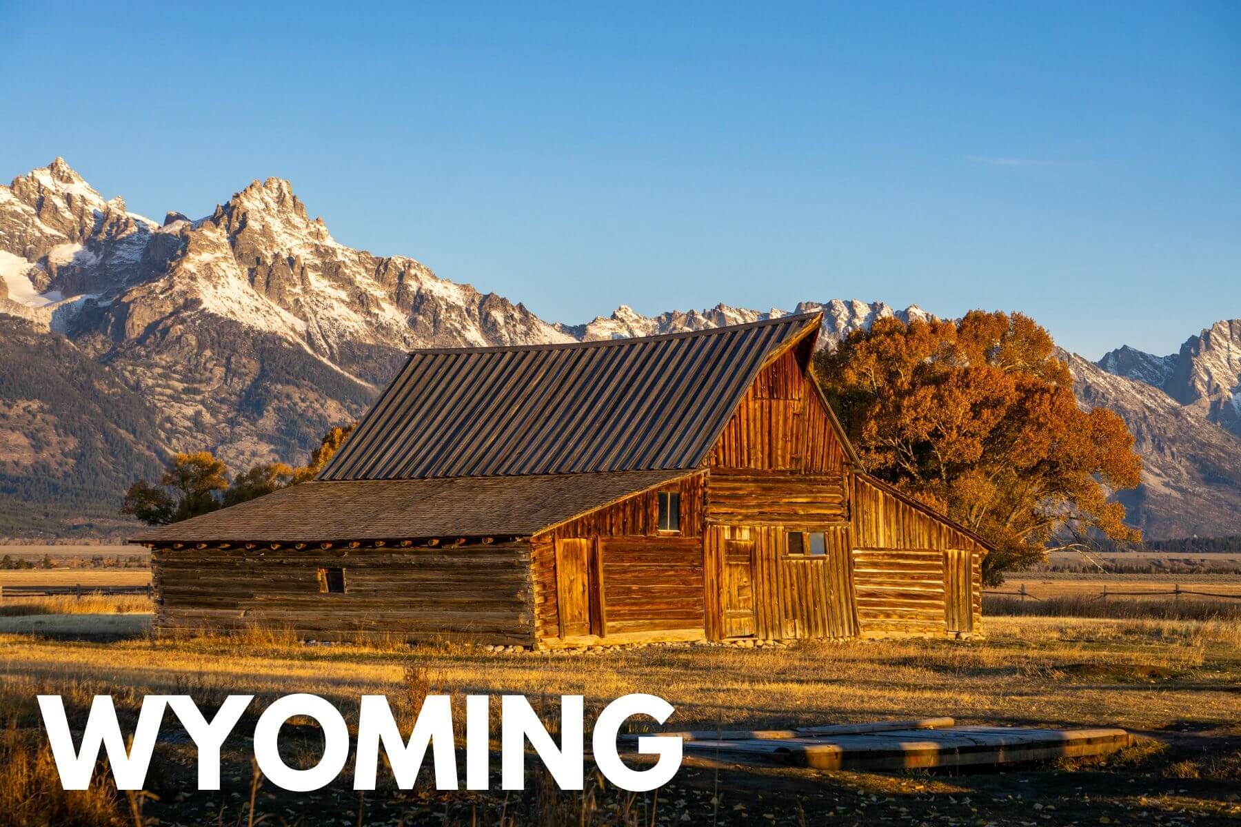 Photo of a wooden barn in a meadow with mountains behind at sunset and the word Wyoming overlaid