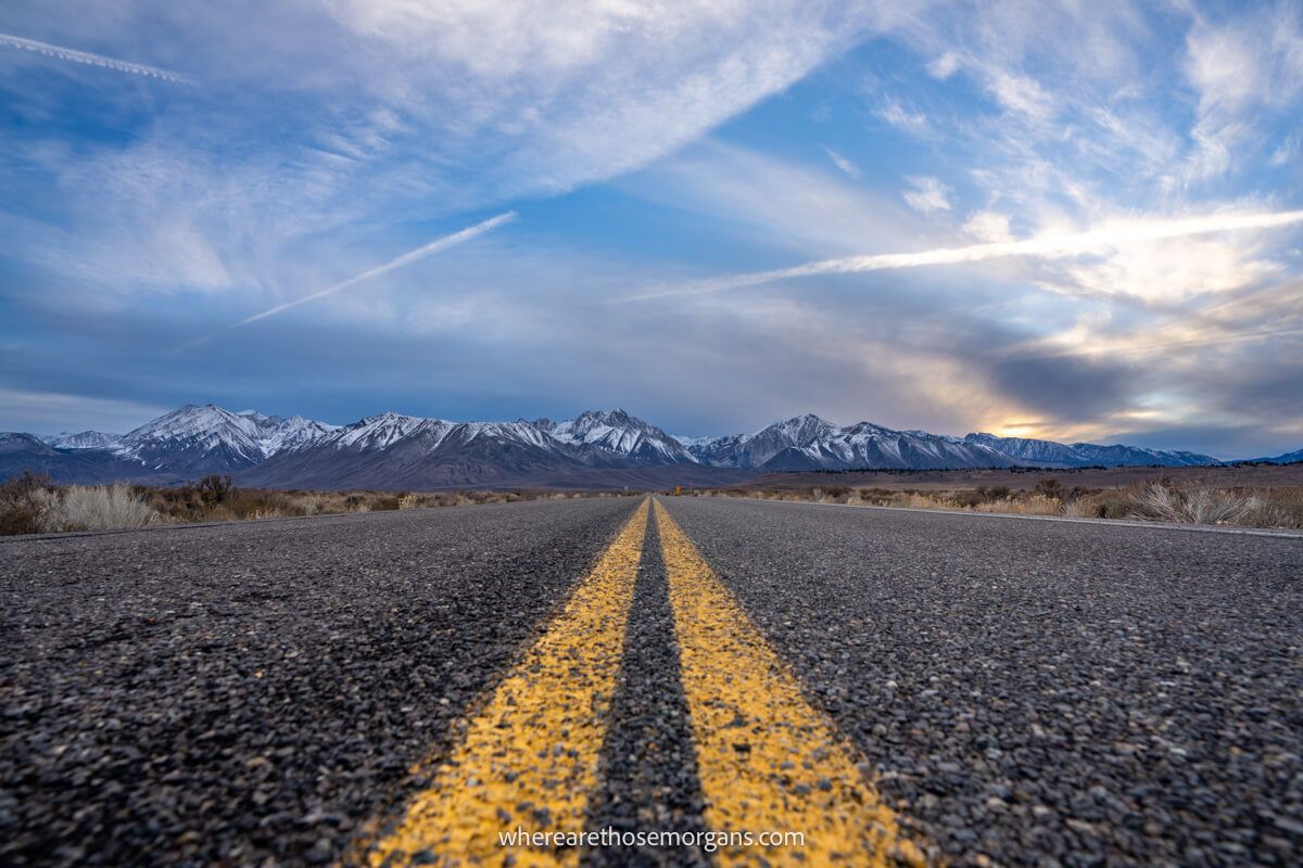 Close up view of a long stretch of road with snow covered mountains in the distance